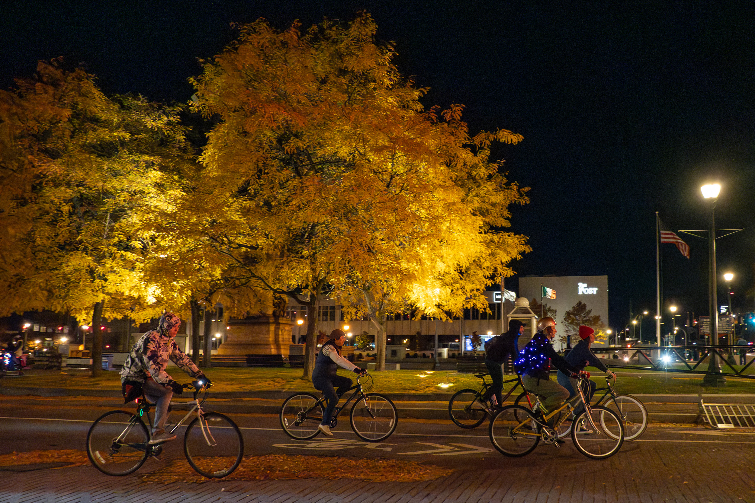 Five cyclists riding down a Syracuse street at night.