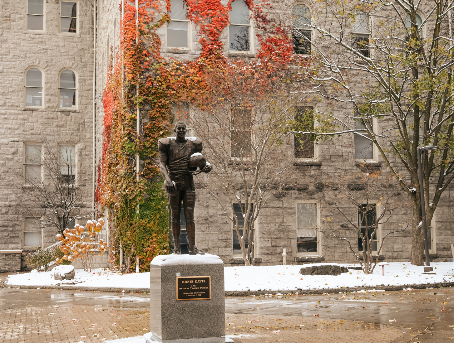 The Ernie Davis statue stands framed by ivy and light snow outside SU’s JMA Wireless Dome, marking the arrival of snowy days.