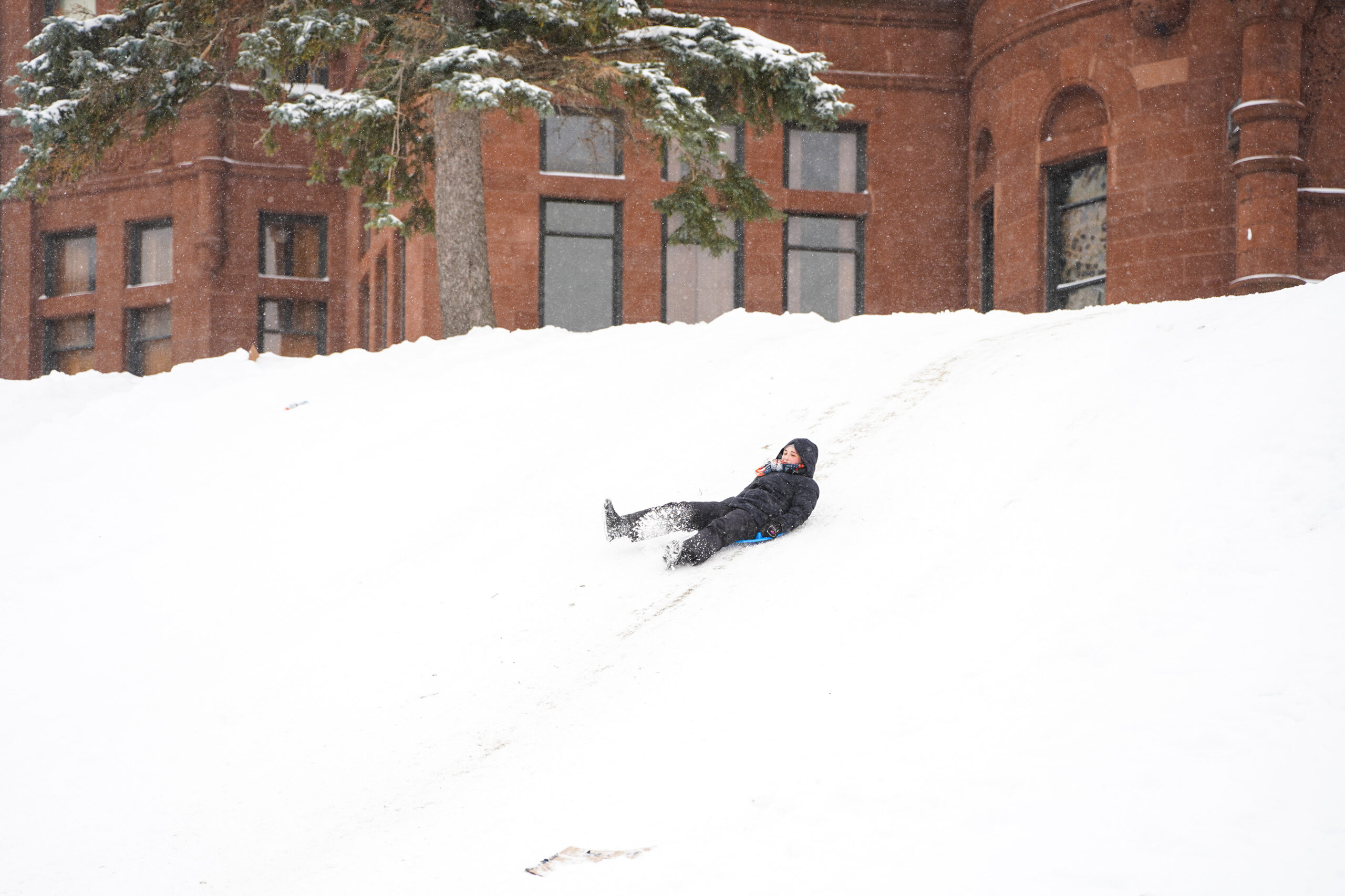 An SU student sleds down Crouse hill. Virtual classes sent students into a sled-day frenzy on the freshly coated hill.